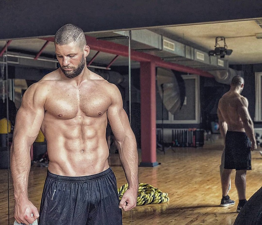 Florian Munteanu standing shirtless in a training room looking muscular and fit