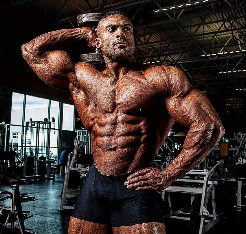 Henri-Pierre Ano lifting a dumbbell while being shirtless, looking ripped and muscular