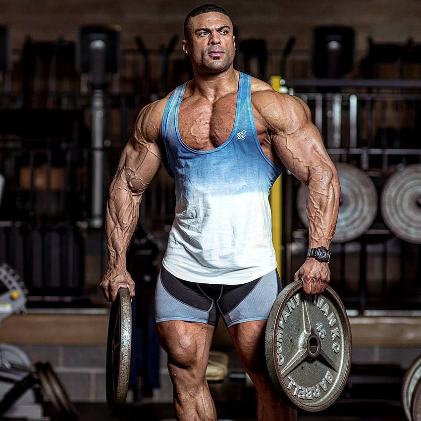 Henri-Pierre Ano holding a weight plate wearing a tank top looking fit and muscular