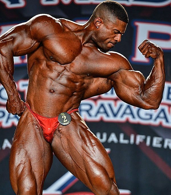 Henri-Pierre Ano flexing his biceps on a bodybuilding stage