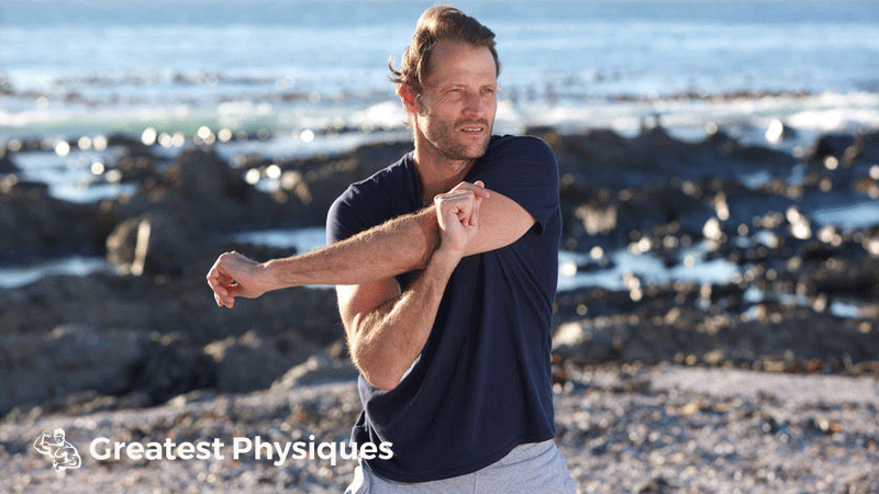 Middle-aged man performing a shoulder stretch on the beach