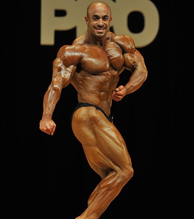 Sasan Heirati doing a 'Phil Heath' iconic side flex pose on a bodybuilding stage