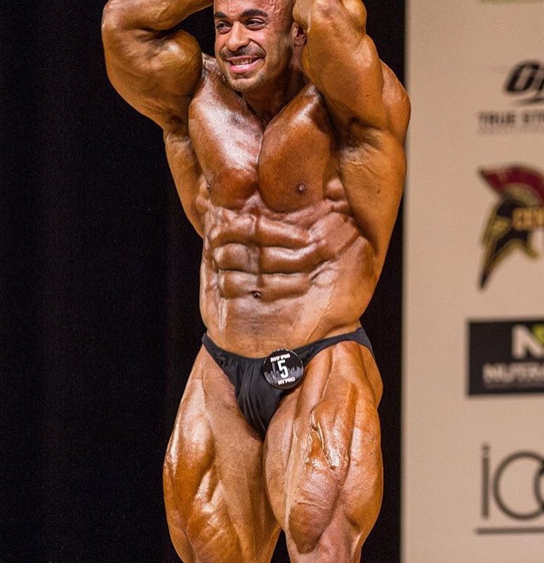 Sasan Heirati doing an ab and leg most muscular pose on a bodybuilding stage