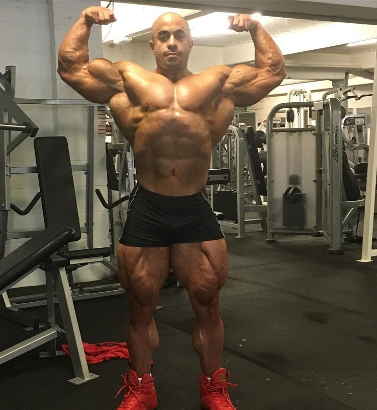 Sasan Heirati doing a shirtless front double biceps pose in a gym