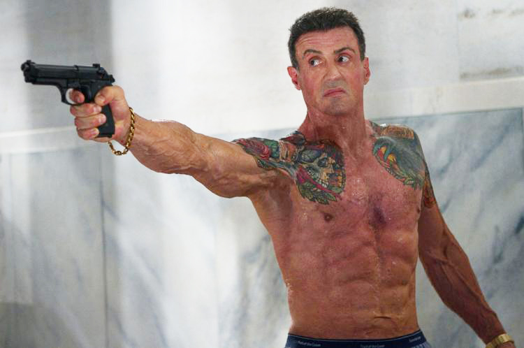 Sylvester Stallone holding a gun shirtless in a film looking lean and muscular