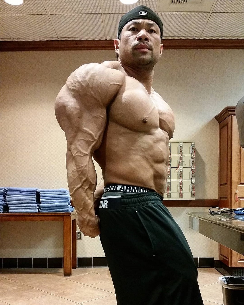 An Nguyen performing a side triceps pose for a camera looking huge