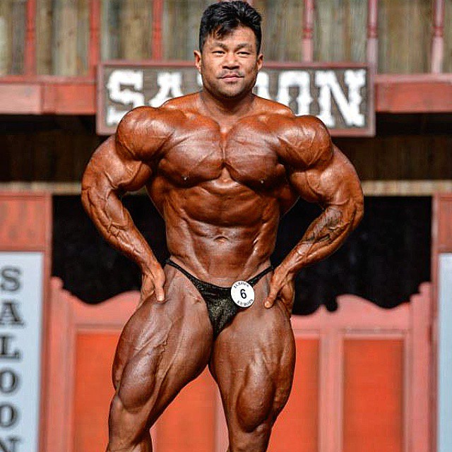 An Nguyen doing a most muscular pose on a bodybuilding stage looking ripped