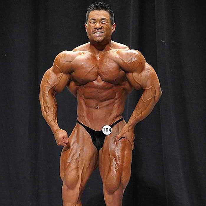 An Nguyen flexing his ripped and conditioned muscles on a bodybuilding stage