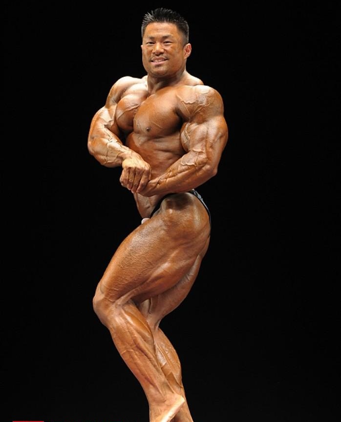 An Nguyen showing off his side chest pose on a bodybuilding stage