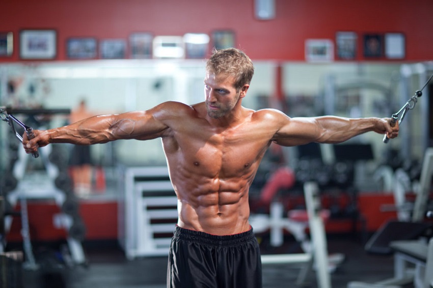 Ben Booker doing cable crossovers while being shirtless in the gym, looking ripped