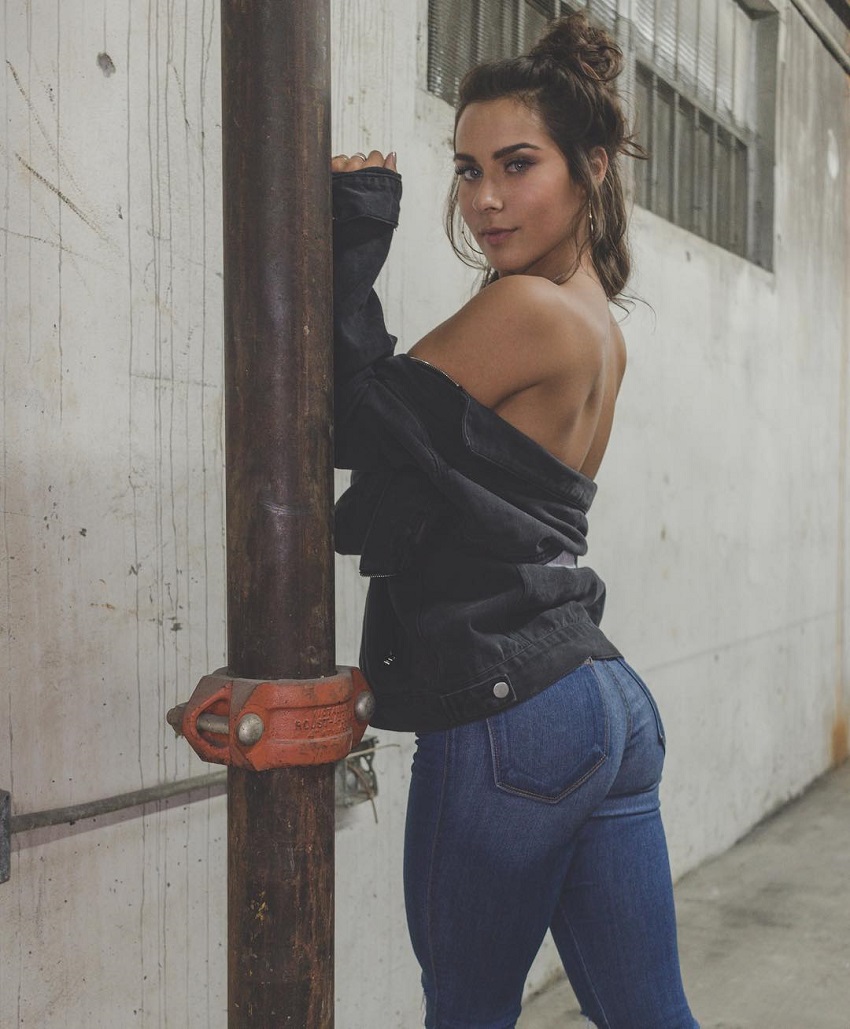 Janeece Sinclair posing in blue jeans and leather jacket showing off her curvy glutes