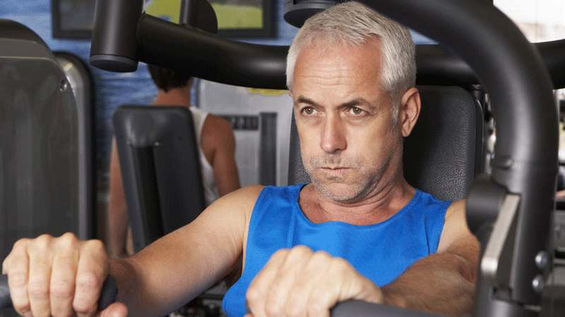 Grey-haired older guy using a chest press in the gym