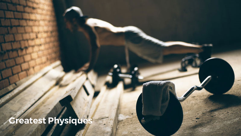 Circuit training male athlete performing push-ups on a bench behind a barbell