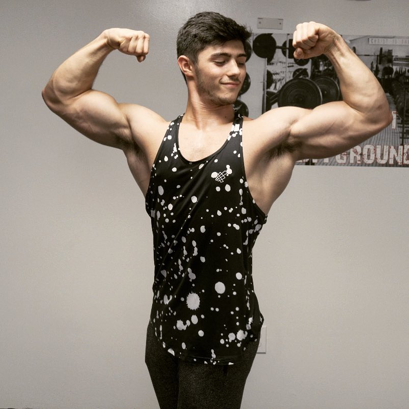 Qwin Vitale doing a front double biceps pose for a photo wearing a black tank top with white spots