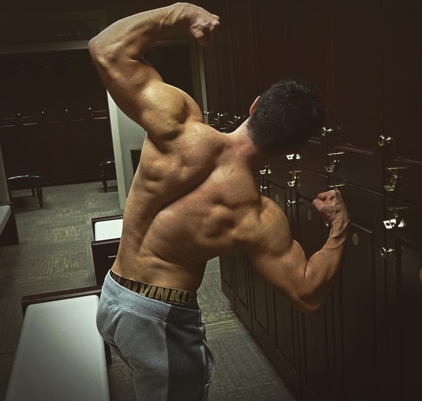 Qwin Vitale flexing his back and arms in a gym locker room