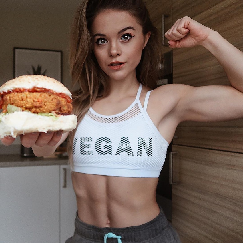 Stefanie Moir posing for a photo with a vegan burger in her hand looking fit and healthy