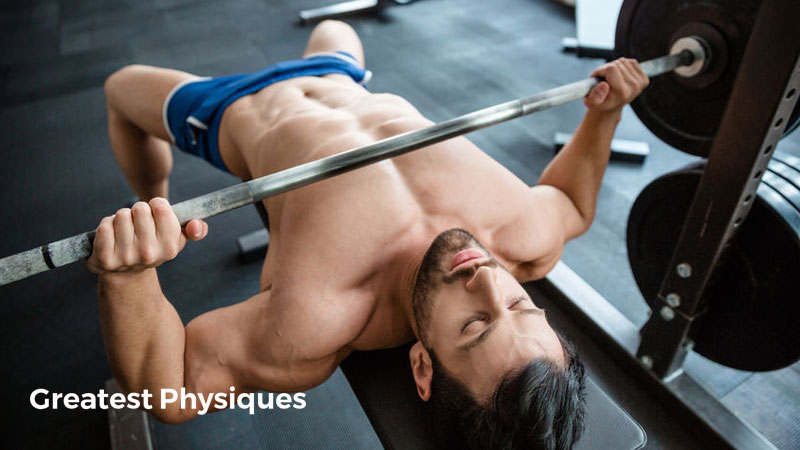 Lean and muscular bodybuilder in blue shorts performing bench press in the gym