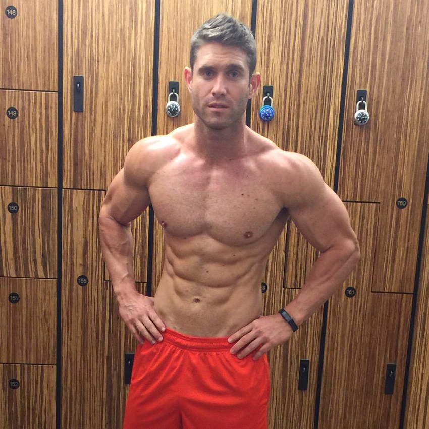 CJ Koegel posing shirtless in a gym locker room looking ripped and lean