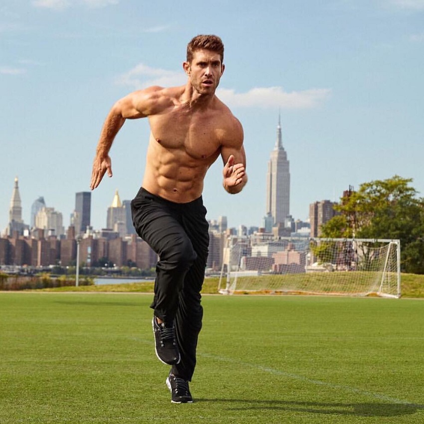 CJ Koegel running shirtless on a grass field looking big and ripped