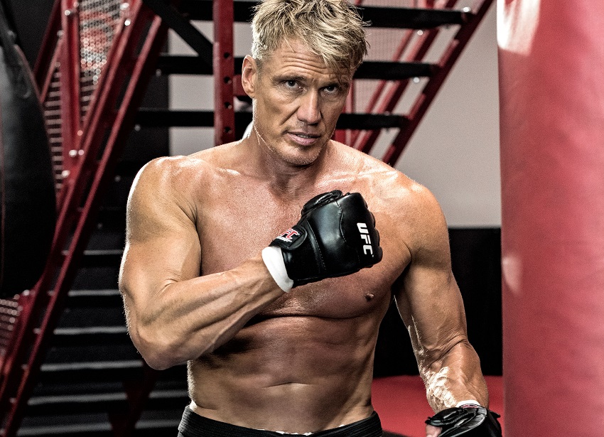 Dolph Lundgren posing shirtless and waring black boxing gloves looking ripped