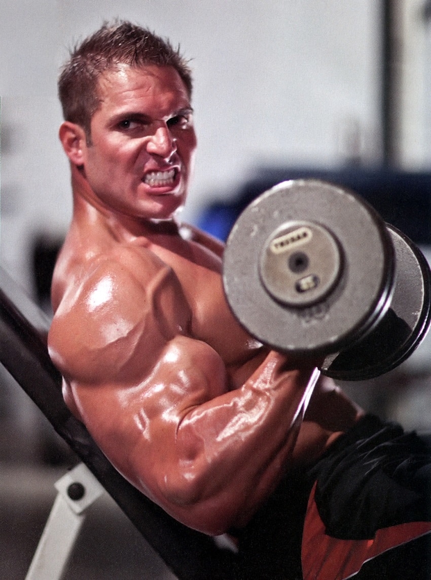 Josh Bergeron doing seated biceps curls with a grimace, looking big and ripped