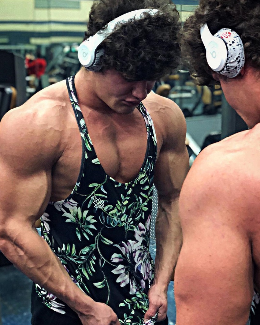 Justin Martilini standing in a gym by a mirror wearing white headphones getting 'pumped' for a workout