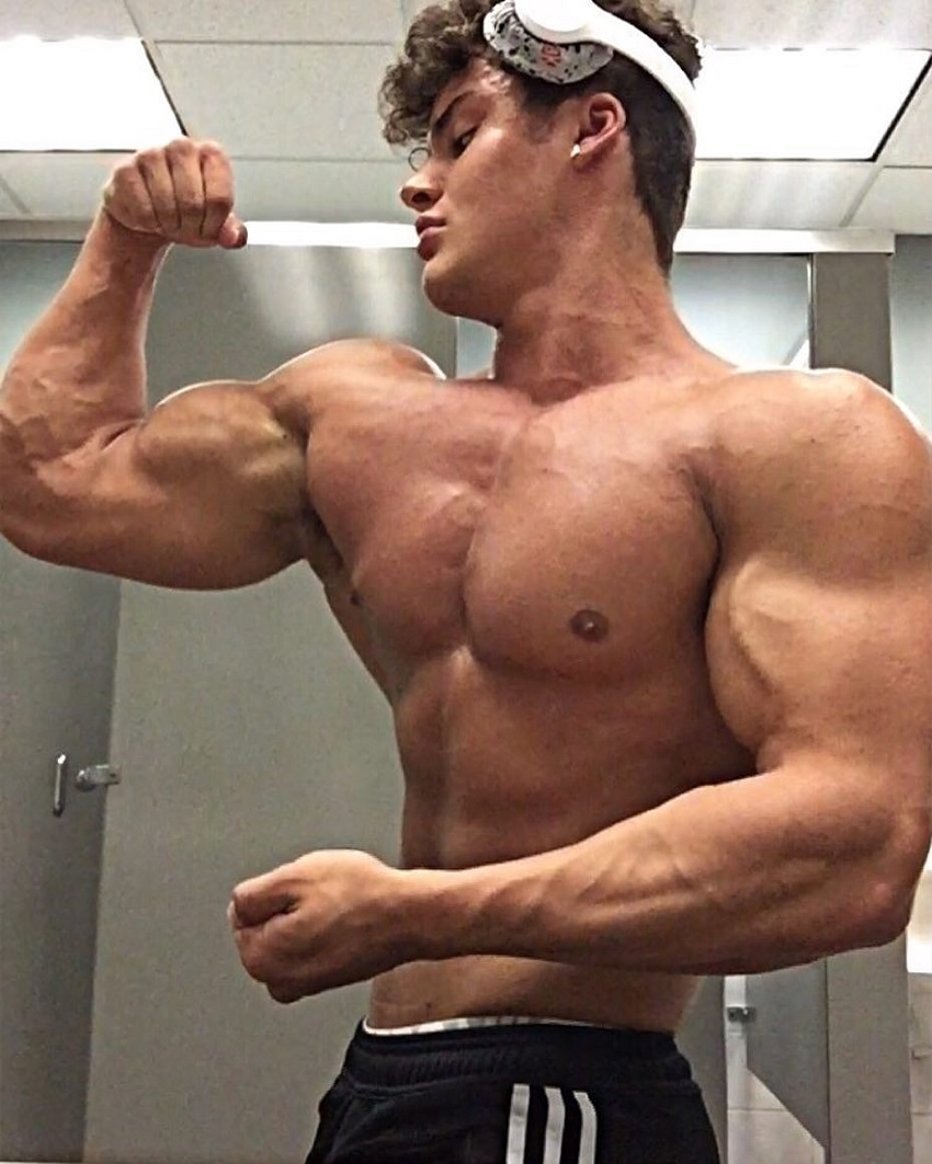 Justin Martilini standing shirtless flexing his bulging biceps in a photo