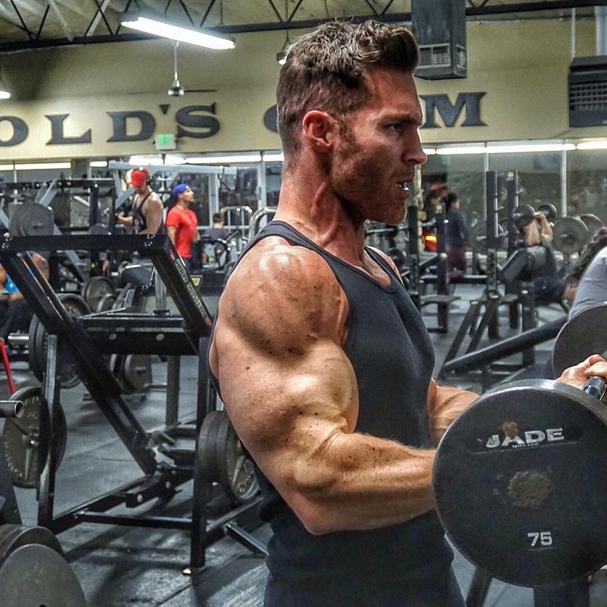 Kyle Clarke performing heavy barbell curls, his arms looking huge and ripped