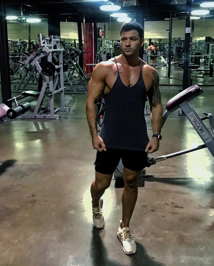 Rob Sharpe standing in a gym wearing a black tank top looking big and ripped