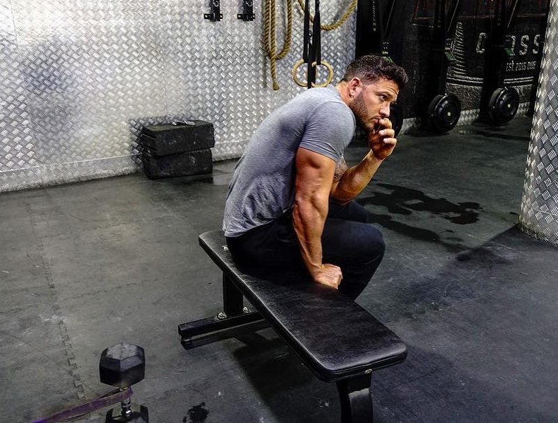 Rob Sharpe sitting on a bench showing off his ripped and muscular triceps