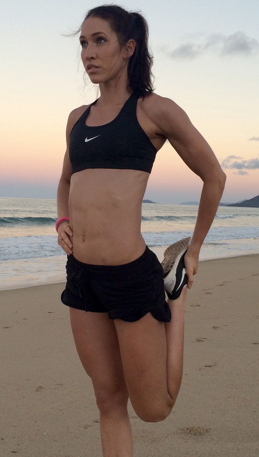 Cass Olholm stretching on the beach in her sports suit