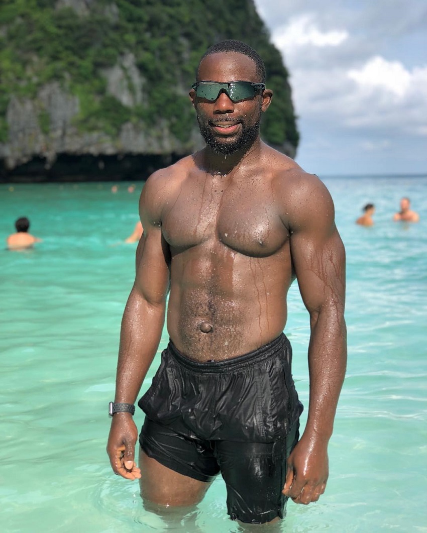 Gideon Akande standing shirtless in the light blue sea looking ripped and muscular