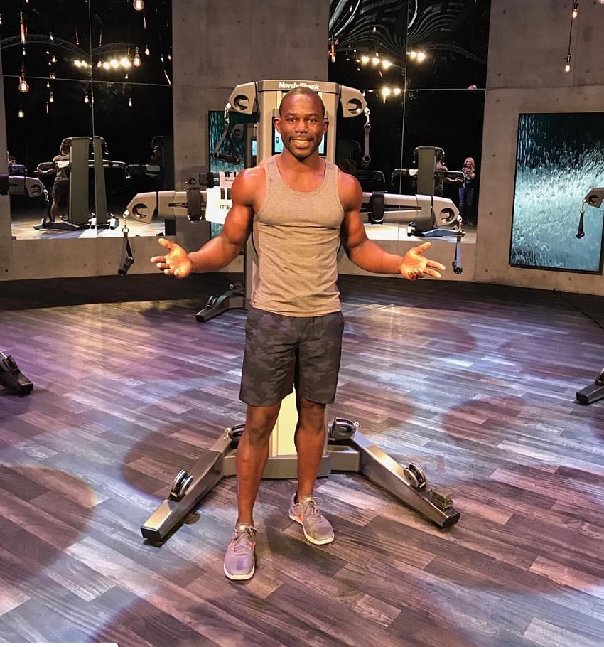 Gideon Akande standing in a grey tank top showing off his lean physique