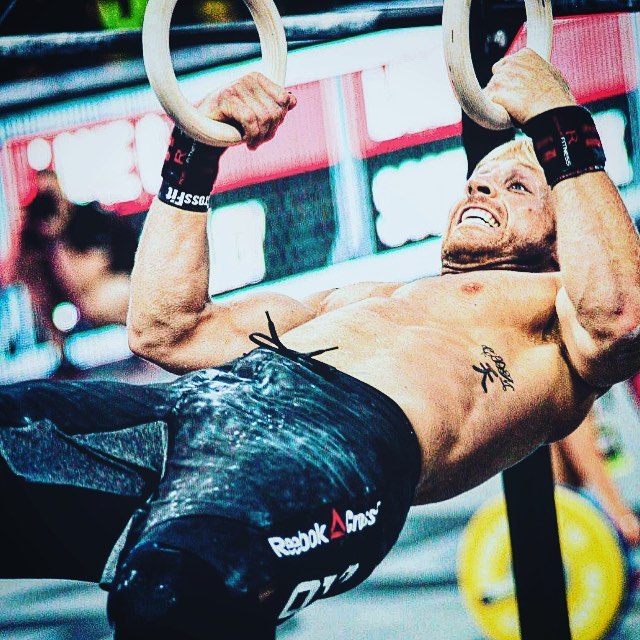 Graham Holmberg hanging on rings with his hands during a CrossFit competition