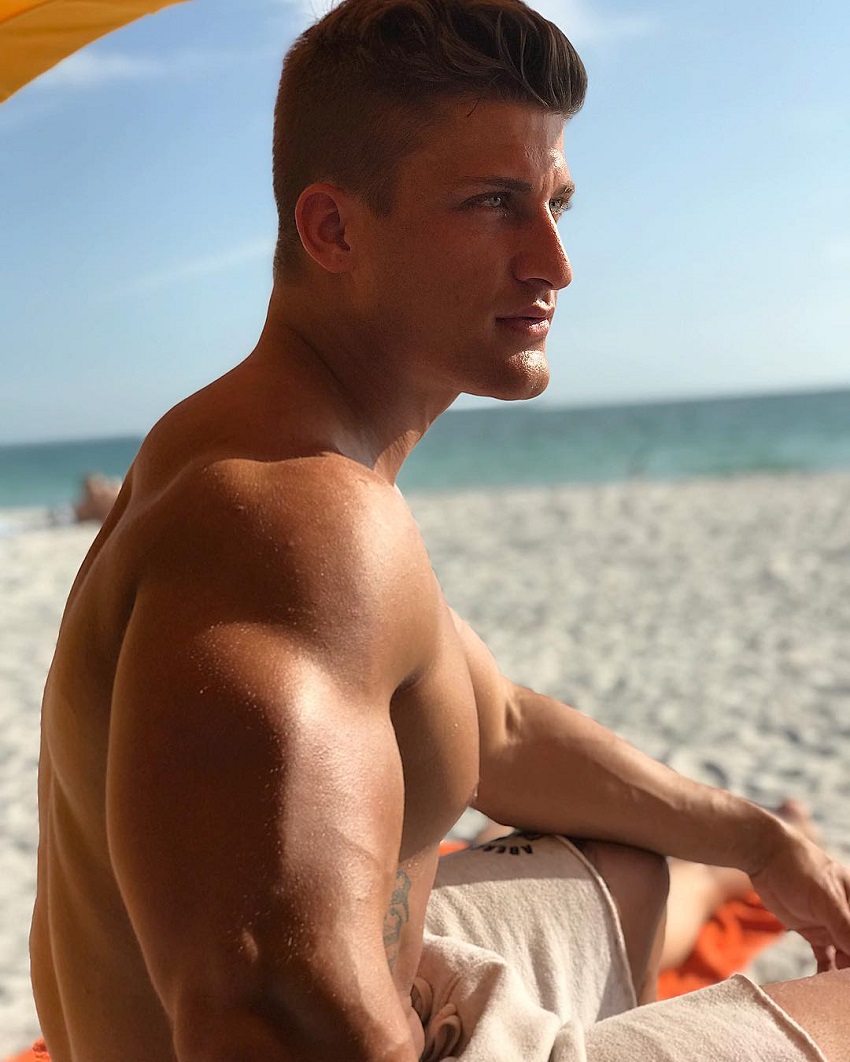 Quinn Biddle sitting on a beach posing for a photo, looking strong and lean