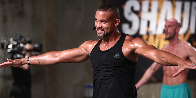 Shaun T during a fitness boot camp wearing a black tank top, looking fit anad muscular