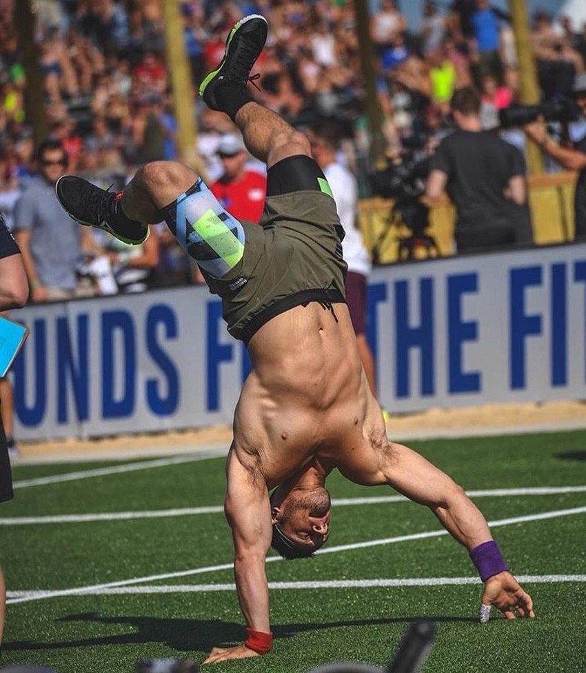 Travis Williams doing a handstand during a CrossFit competition, looking strong and lean