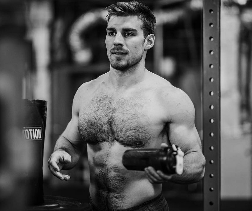 Alex Anderson shaking his shaker bottle after training, his shirtless body looking strong and ripped