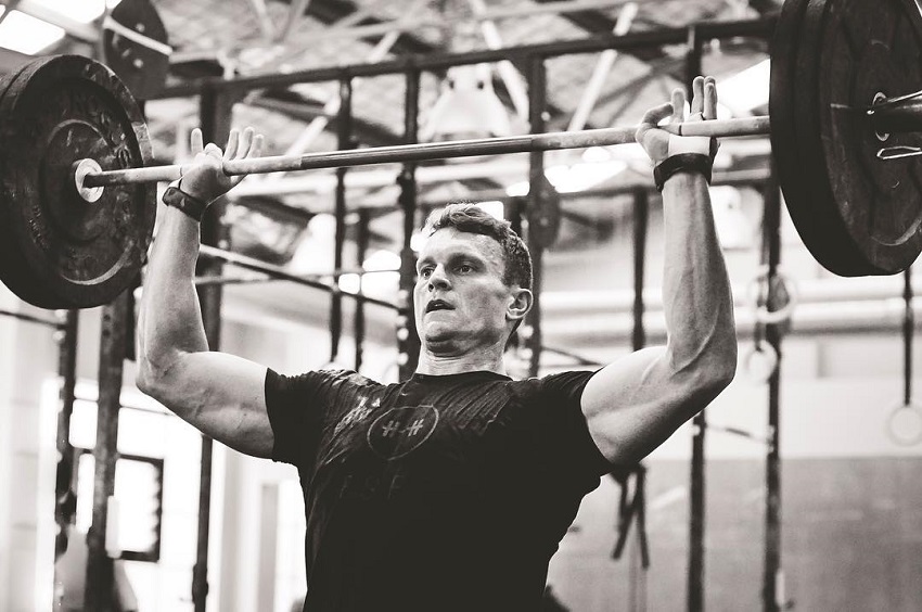 Chad Mackay doing a seated overhead barbell press, looking strong