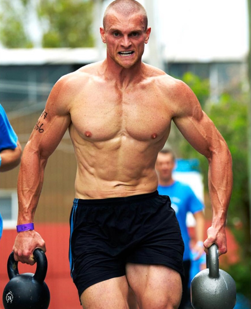 Chad Mackay running shirtless with kettlebells in his hands during a CrossFit event