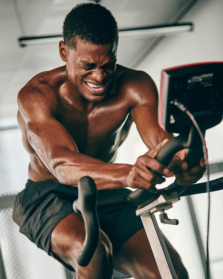 Joe Holder doing cardio on a stationary bike with a pained grimace