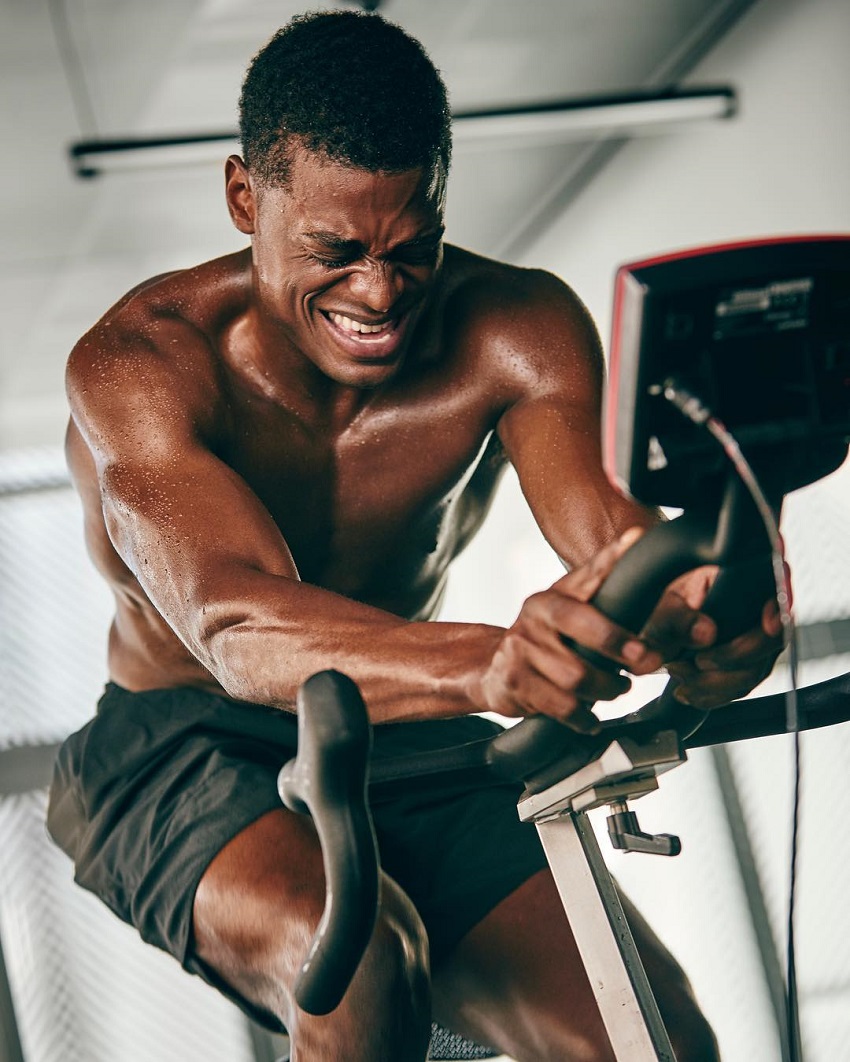 Joe Holder doing cardio on a stationary bike with a pained grimace