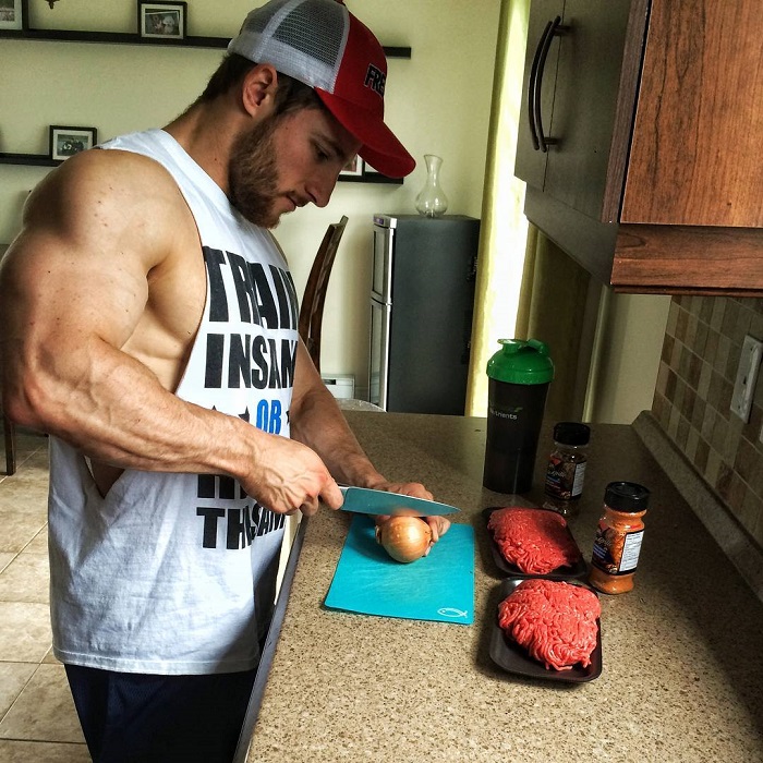Jonathan Plante wearing a white tank top, cutting meat in the kitchen