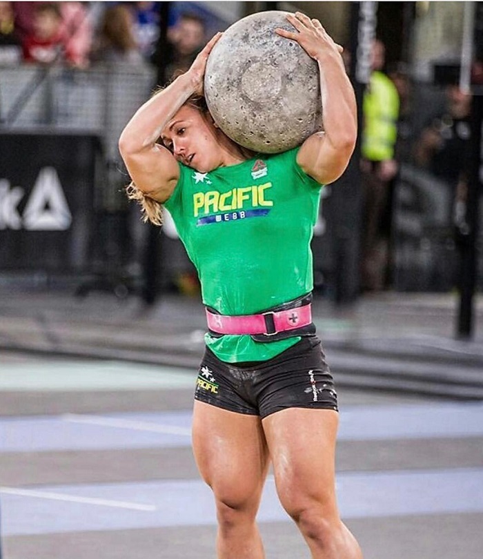 Kara Webb Saunders lifting a heavy rock boulder her legs looking big and aesthetic