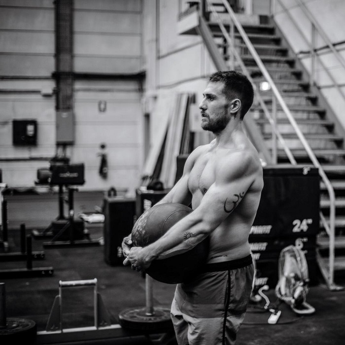 Khan Porter posing shirtless while lifting a heavy medicine ball