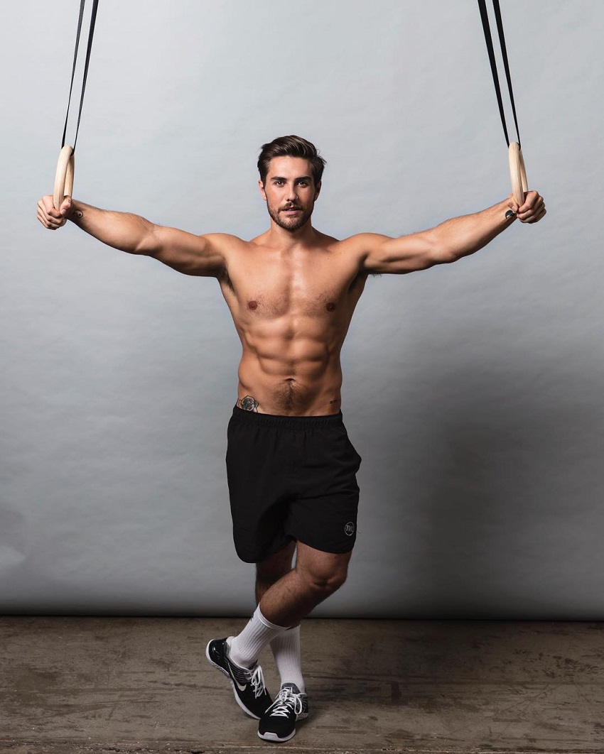 Khan Porter posing for a photo standing shirtless with the rings in his hands