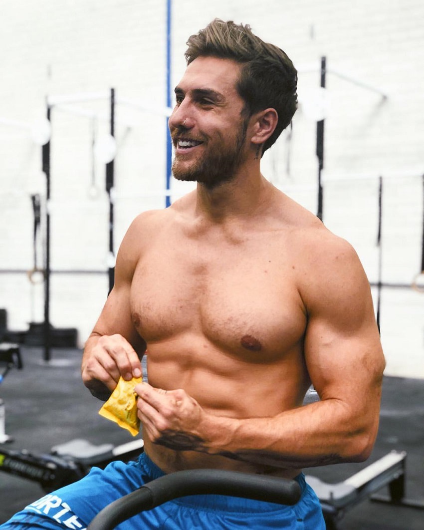 Khan Porter eating a snack while being shirtless in a CrossFit gym, looking ripped and strong