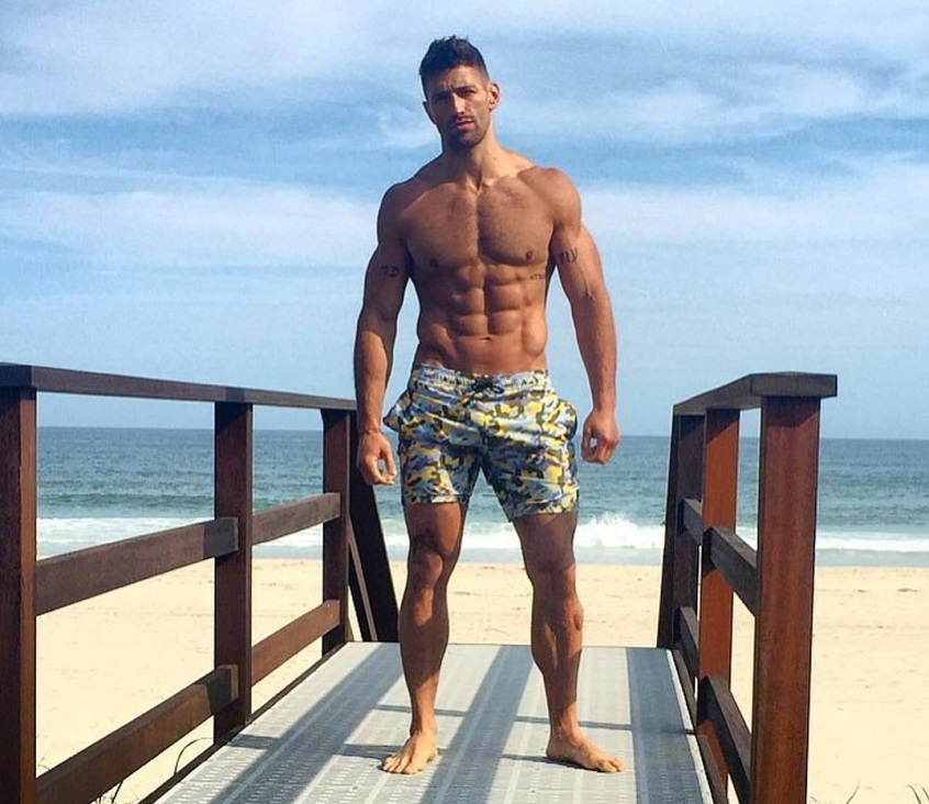 Noah Neiman posing shirtless by the beach looking strong and aesthetic