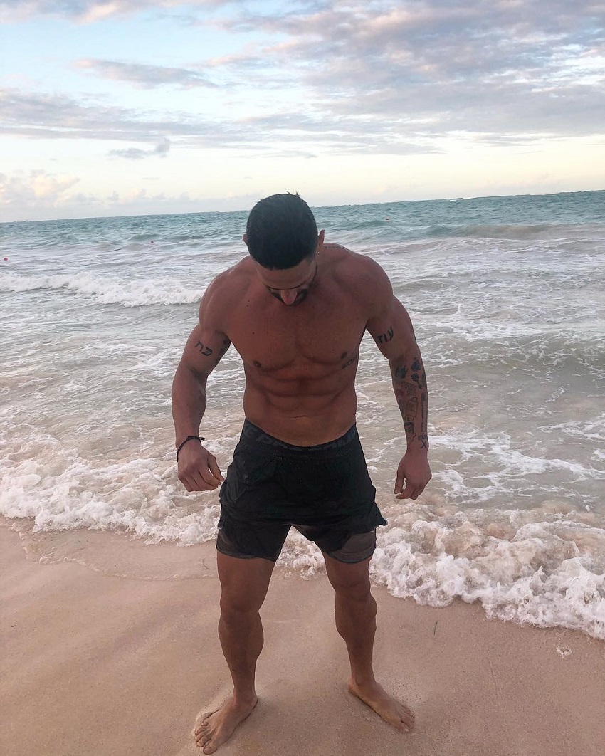 Noah Neiman posing shirtless on the beach looking strong and fit