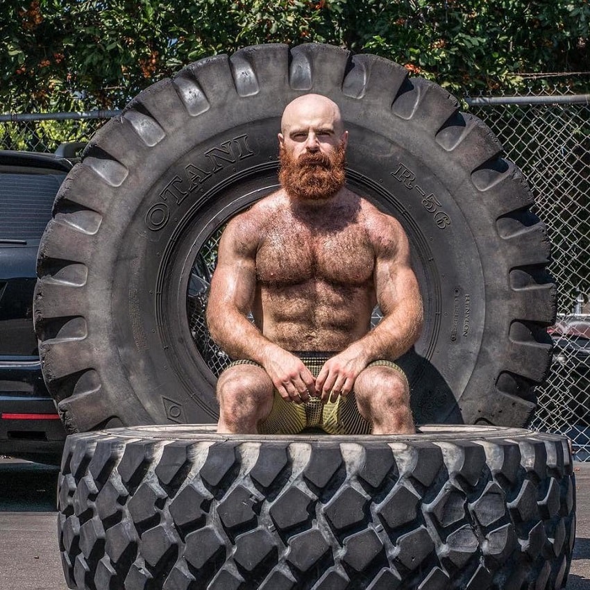 Lucas Parker sitting shirtless on a big tire, looking muscular